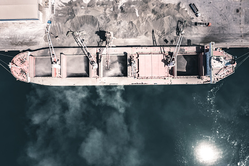 Aerial view of a large cargo ship being loaded with cement in an international port. Sea transportation. Cinematic view.