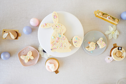 An Easter cake and small Easter cupcakes shaped like Easter bunnies, Easter chicks and Easter eggs. Served together with modern patisserie and table decoration. Photographed in high resolution