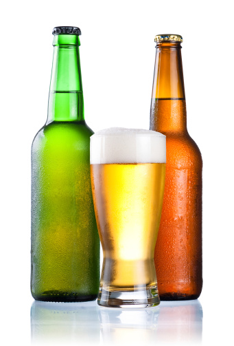 Brown and green bottles full of condensate and covered with a glass of fresh cold beer isolated on a white background