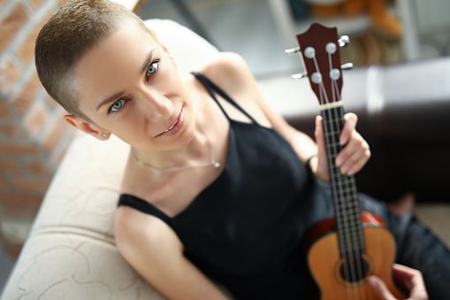 Top view of person playing melody on ukulele. Pretty female elegant hand pressing on string. Musical talent. Simple black dress on artist. Musical instrument and hobby concept