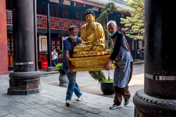 成都、中国 - 2022年5月7日:成都の温州僧院で仏陀の誕生日式を準備するために、2人の信者が仏像を運んでいます - many colored prayer flags ストックフォトと画像