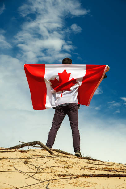 A man with a Canadian flag stands on the sand, skies on the background. stock photo