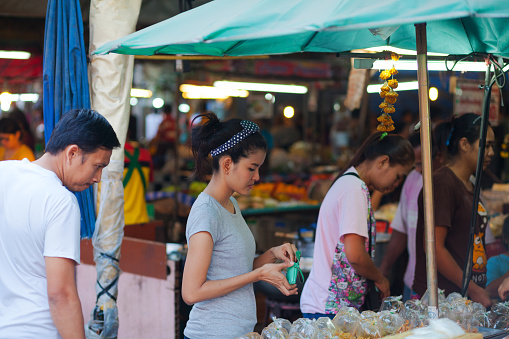 Thai people are shopping on  local market in Bangkok Chatuchak near CRU university. In center is a young woman. View into market and market stalls with people