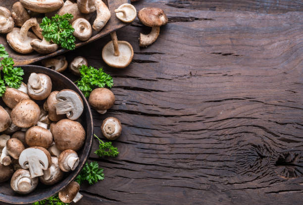 istock Different brown colored edible mushrooms on wooden table with herbs. Top view. 1395910295