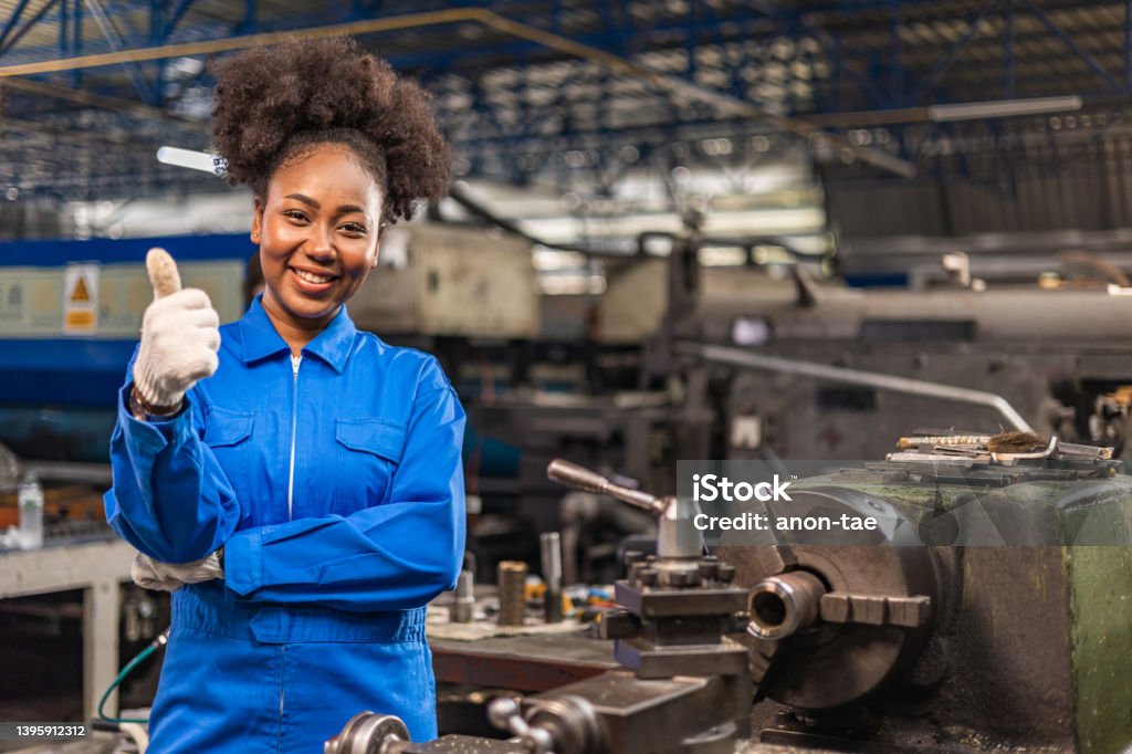 African American Young woman worker  in protective uniform operating machine at factory Industrial.People working in industry.Portrait of Female  Engineer looking camera  at work place. Mechanic Stock Photo