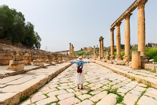 young woman tourist in color dress and hat leading man to South gate of the Ancient Roman city of Gerasa, modern Jerash, Jordan. Traveling together.