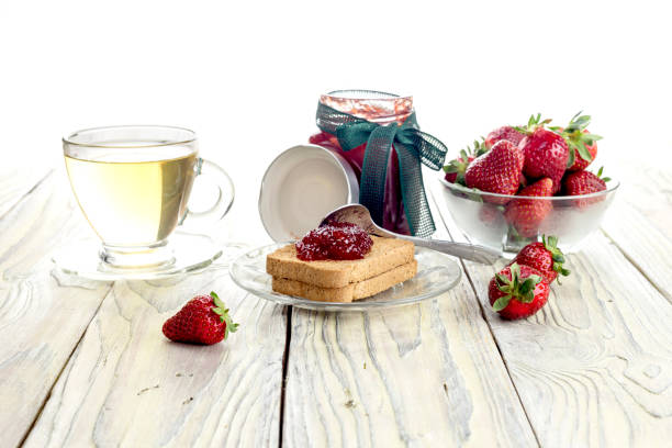 Strawberry jam, rusks and tea in a cup on a wooden table close-up