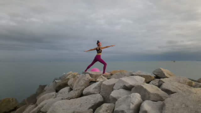 Woman exercising and meditating yoga exercise outdoors by the sea .