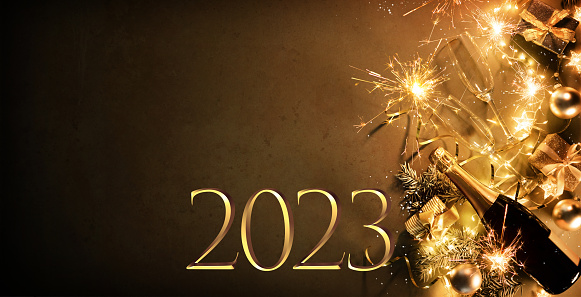 New Years Eve holiday background with fir branches, number 2023, champagne bottle, christmas balls, gift box and lights on dark board