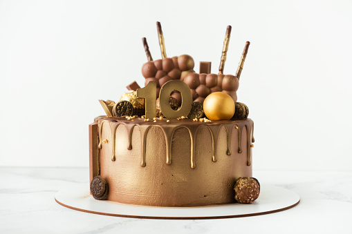 Luxury birthday chocolate cake with drips decorated with candies covered with brown and golden cream cheese frosting