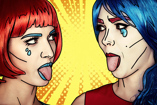 Portrait of young women in comic pop art make-up style. Females in red and blue wigs on yellow - orange cartoon background. Girls show each other tongues