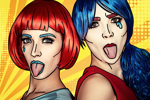 Portrait of young women in comic pop art make-up style. Females in red and blue wigs on yellow - orange cartoon background. Girls show each other tongues