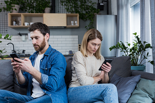 Conflict, quarrel. Man and woman, couple, family sitting on the couch with their backs to each other with phones, do not talk to each other, do not pay attention, busy with phones