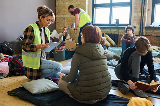 Voluntaria con dispositivos móviles sentada en cuclillas frente a un refugiado photo