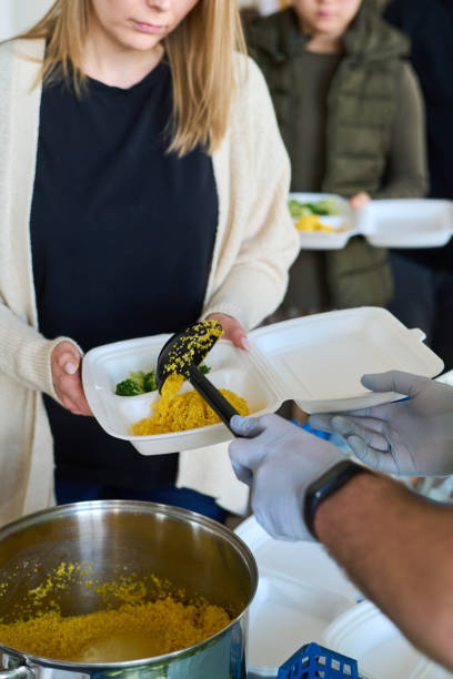 istock Young blond female refugee holding plastic container over pan with pilaf 1395923286