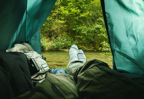 A man is lying in a tent and looking at the beautiful landscape in nature.