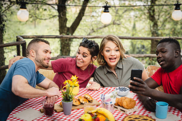 istock happy friends having breakfast in the backyard, young influencer using smartphone to create content on social media with photos of food, multiracial couples having fun at picnic outside 1395928924