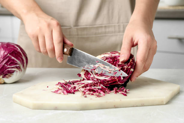 femme coupant du radicchio mûr frais à une table légère, gros plan - radicchio photos et images de collection