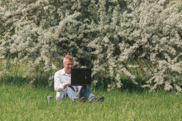 Adult man working online outdoors in the city park, drinking coffee from reusable coffee mug