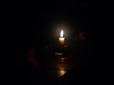 Close-up photo of a candle flame seen in a dark room and frangipani flowers next to it