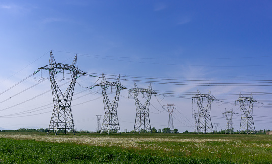 High voltage power pylon lines, high voltage electrical transmission towers on green meadows and blue sky, copy space