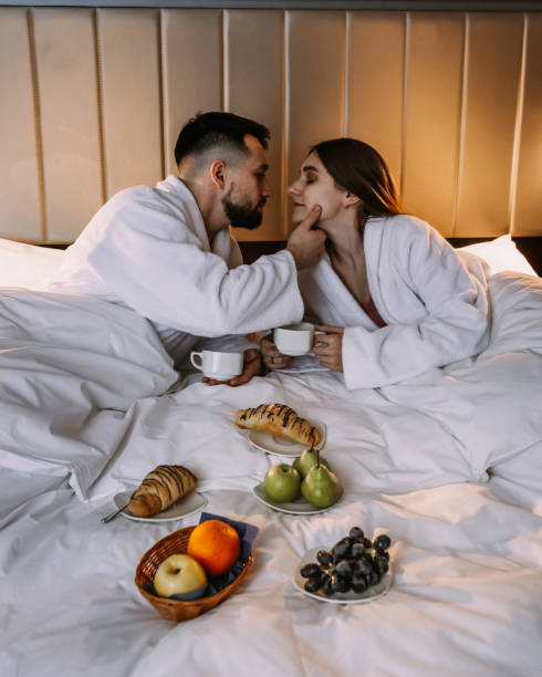 Happy young couple sitting in bed in morning and having breakfast stock photo