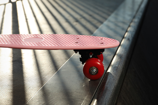 Modern pink skateboard with red wheels on top of ramp outdoors, closeup