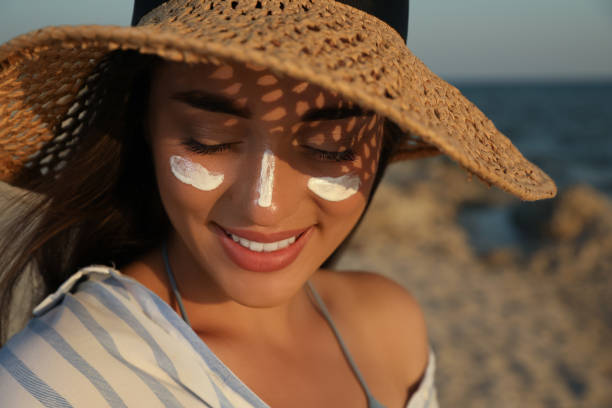 giovane donna felice con la crema di protezione solare sul viso alla spiaggia - crema solare foto e immagini stock