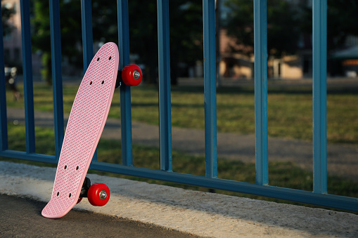 Modern pink skateboard near fence outdoors. Space for text