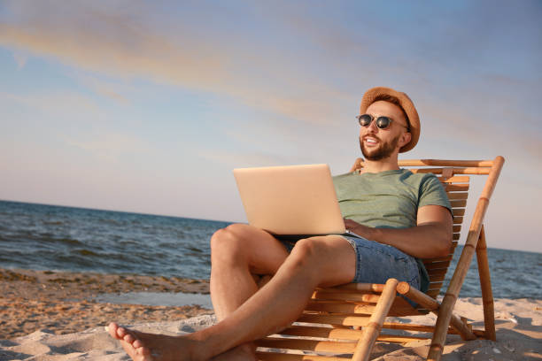 ビーチのデッキチェアでラップトップで作業している男 - on beach laptop working ストックフォトと画像
