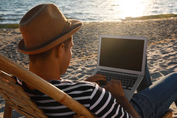 istock Man working with laptop in deck chair on beach 1395934569