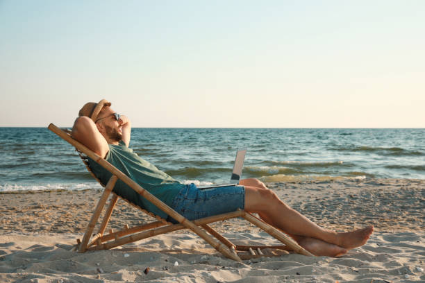 istock Man with laptop relaxing in deck chair on beach 1395934583