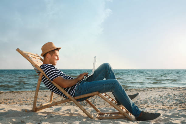 istock Man working with laptop in deck chair on beach 1395934599