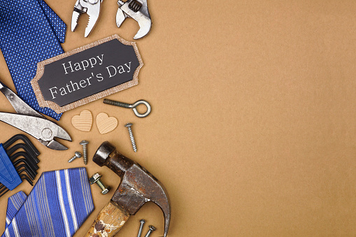 Happy Fathers Day gift tag with side border of ties and tools on a brown paper background. Overhead view with copy space.