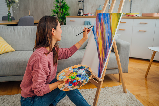 Creative young Japanese woman painting a picture on canvas at home