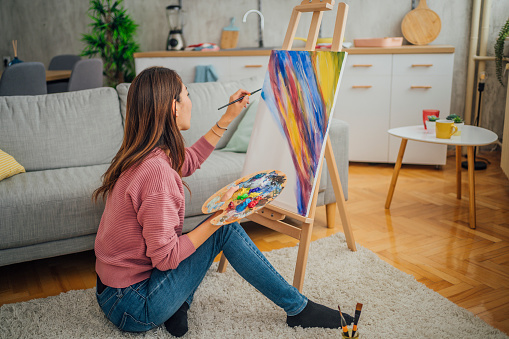 Creative young woman painting a picture on canvas at home