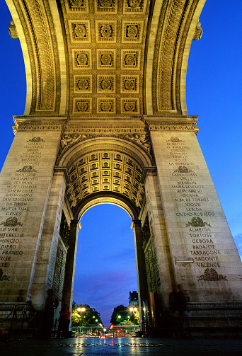 A nocturnal transversal view under the arches of Arc de Triomphe. On the columns are the names of cities where Napoléon’s victorious battles took place; on the ceiling there are 21 sculpted roses.