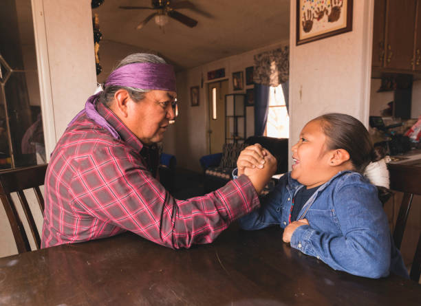 An indigenous Navajo man arm wrestles with his son at the dining room table. Image taken on the Navajo Reservation, Arizona.