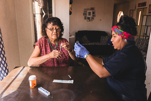 A medical health professional helps a senior indigenous Navajo woman with her medications and health care. Image taken on the Navajo Reservation, Arizona.