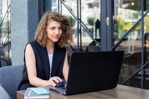 istock young pretty curly haired business woman using laptop and making video call working remote in cafe 1395941509