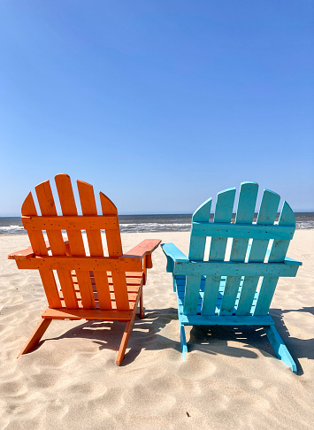 Two beach chairs on a beach facing a still horizon. Horizontal shot.