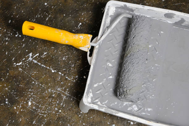 istock Paint roller with yellow handle in tray for roller with gray paint on concrete floor. 1395942091