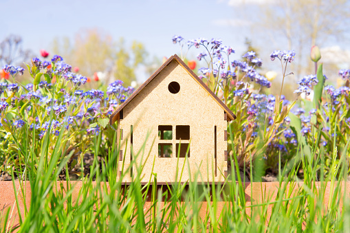 Close-up of a wooden house model standing in a flower bed outdoors. Moving to countryside.