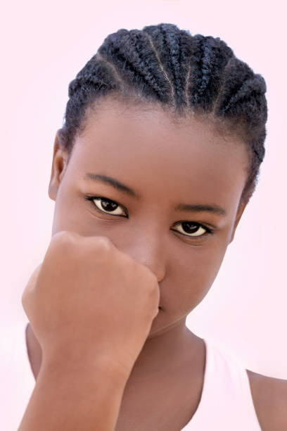 retrato en primer plano de una chica enojada, puño en alto, doce años, fondo rosa claro, foto - anger child braids braided fotografías e imágenes de stock