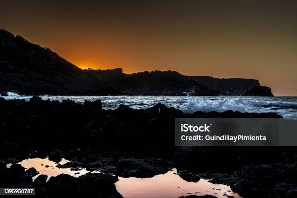 Landscape Of Sunset In A Rocky Beach With Splashing Waves Stock Photo - Download Image Now