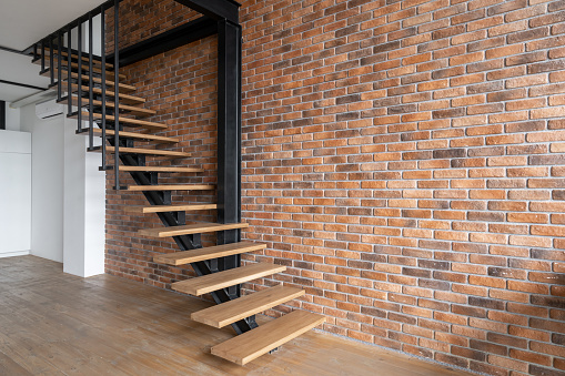 Side view of stairs in cozy loft styled room interior design. New empty apartment for sale with brick wall. Home environment concept. Living room in industrial style