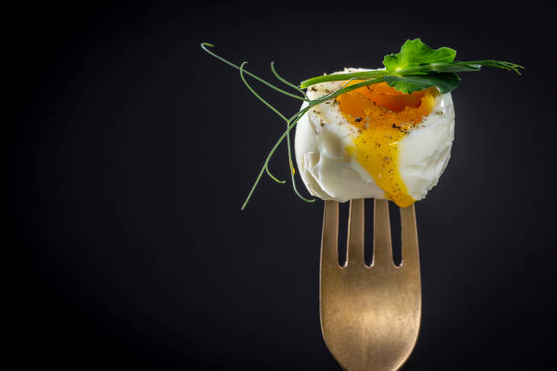 Soft-boiled egg with pea microgreens on a fork on a black background, breakfast time, copy space stock photo