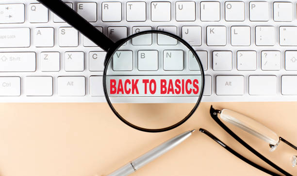 Text BACK TO BASICS on keboard with magnifier , glasses and pen on beige background stock photo