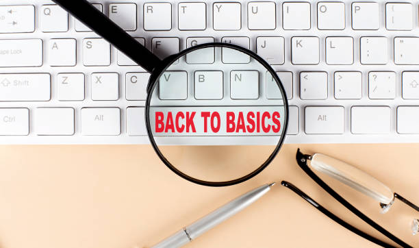 text back to basics on keboard with magnifier , glasses and pen on beige background - simple living imagens e fotografias de stock