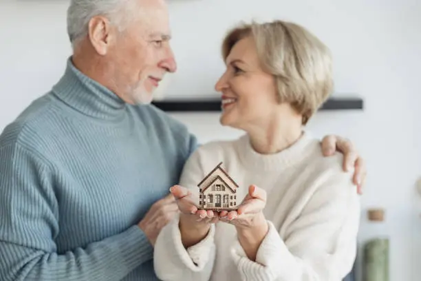 Photo of Couple standing together, while woman holding little house on hands